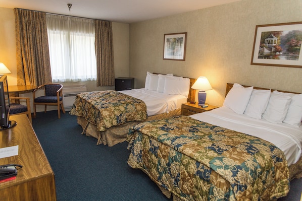 A hotel room with two beds, a desk, a chair, and a window with curtains.