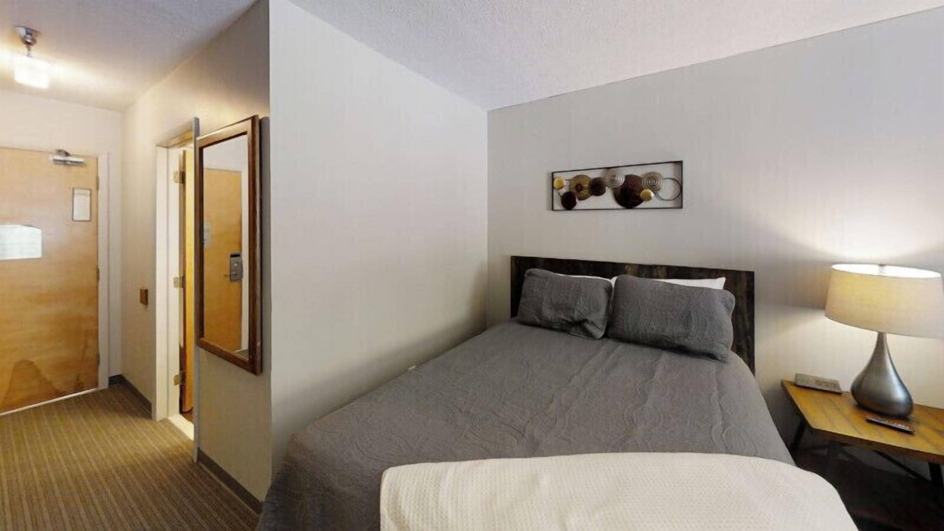 A hotel room with a bed, a bedside table with a lamp, a door, and a wall-mounted artwork.