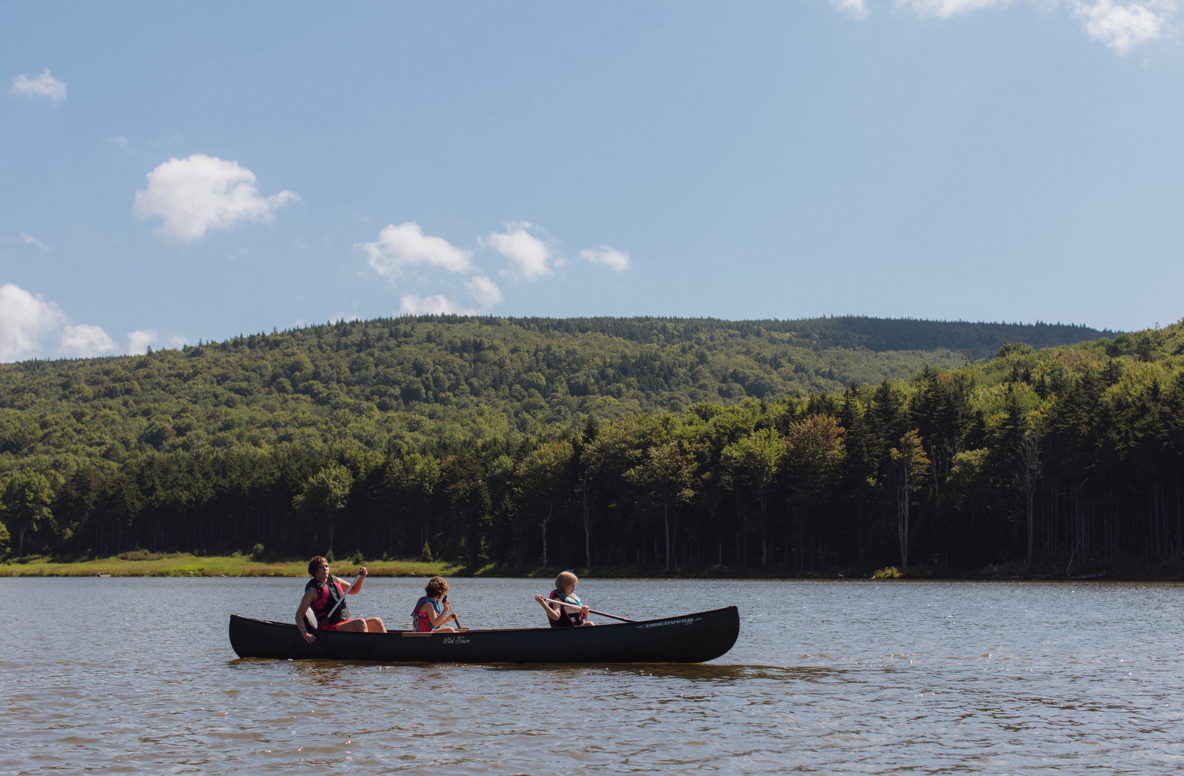 A canoe on a calm lake with a forested hill in the background.