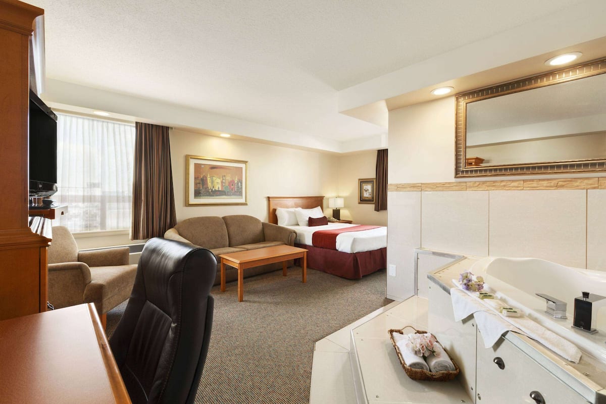 A hotel room with a bed, a sofa, a desk, a television, and a bathroom with a bathtub and mirror.