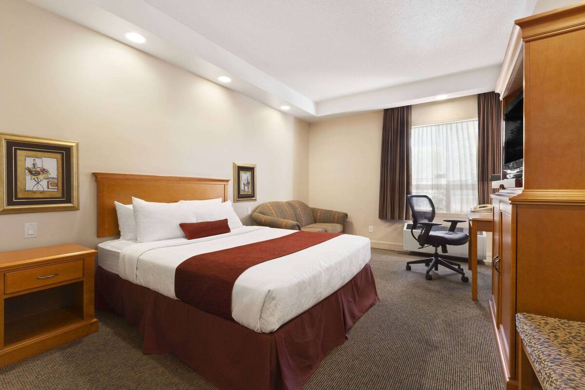 A hotel room with a large bed, a desk, a chair, and a television.