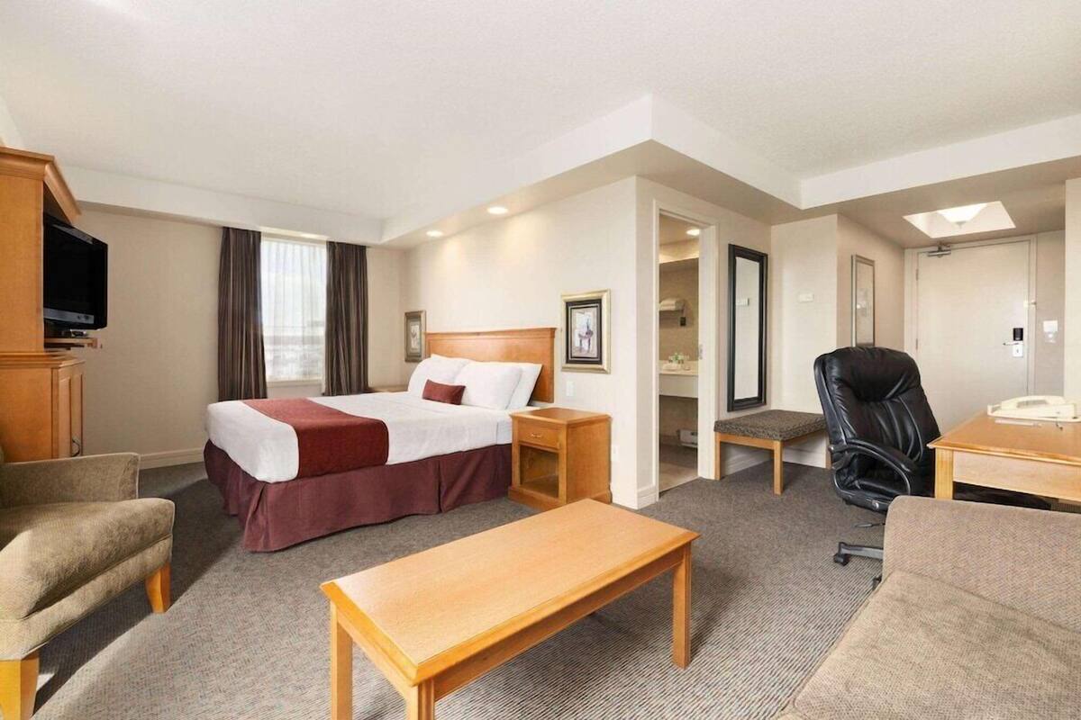 A hotel room with a bed, a desk, a chair, a television, and a small table.