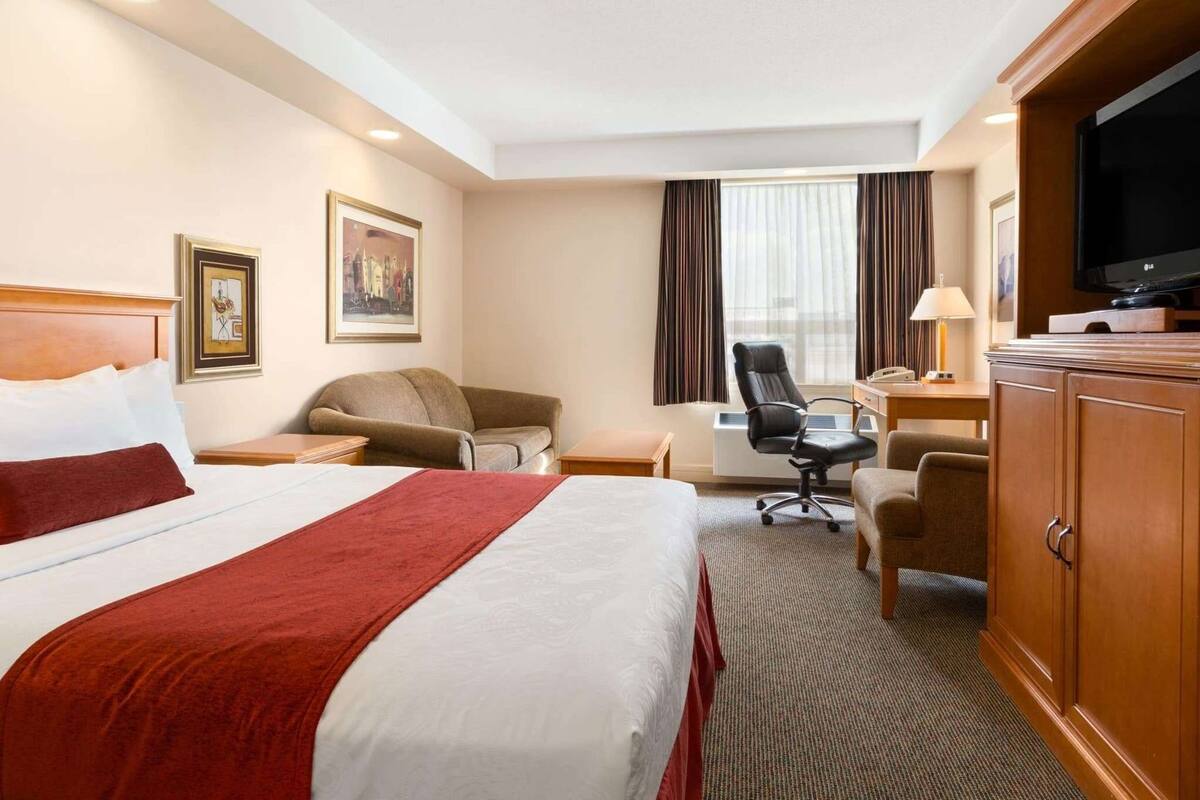 A hotel room with a large bed, a desk, a chair, a television, and a wardrobe.