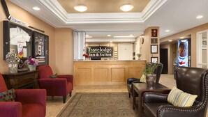Una zona de recepción con un escritorio de madera, sillas de cuero rojo y negro, un cartel grande de Travelodge Inn & Suites y una pared decorativa con premios.