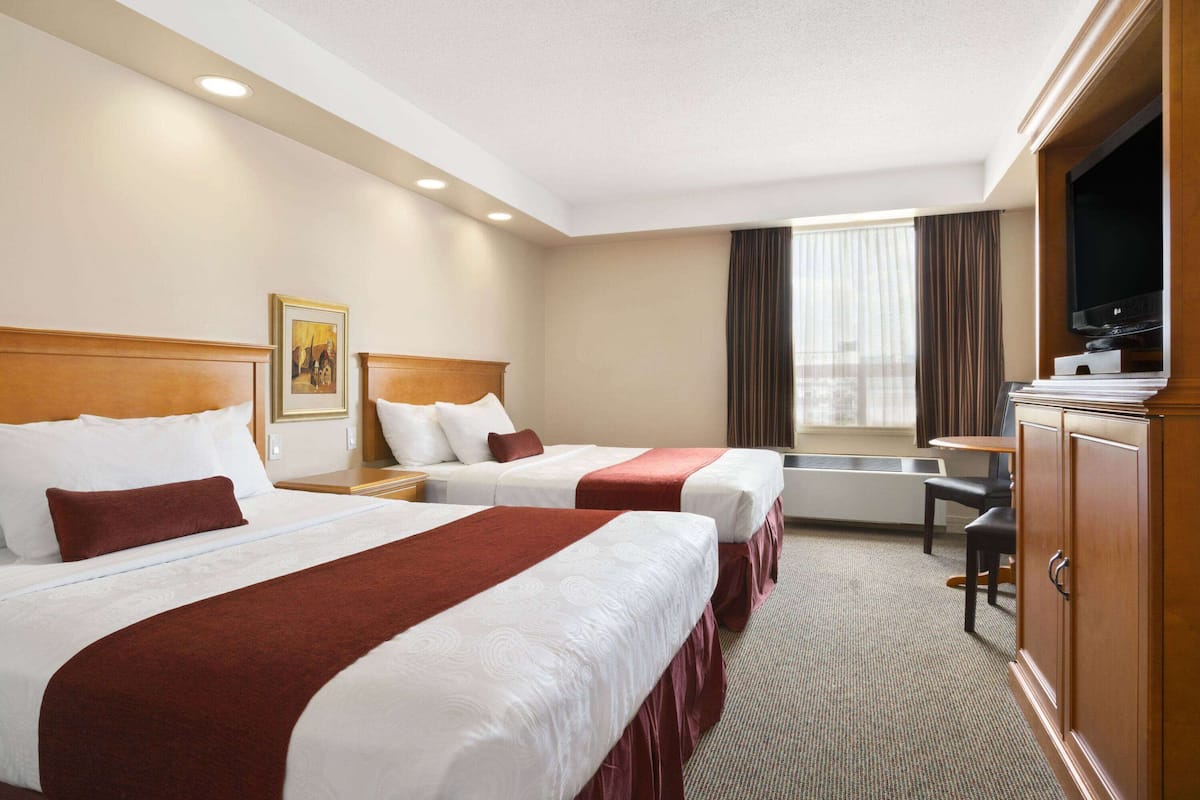A hotel room with two beds, a television, a desk, and a window with curtains.