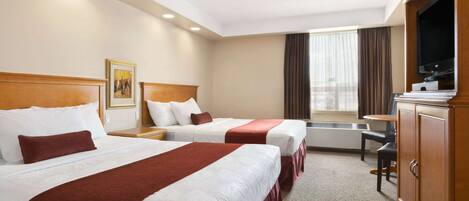 A hotel room with two beds, a television, a desk, and a window with curtains.