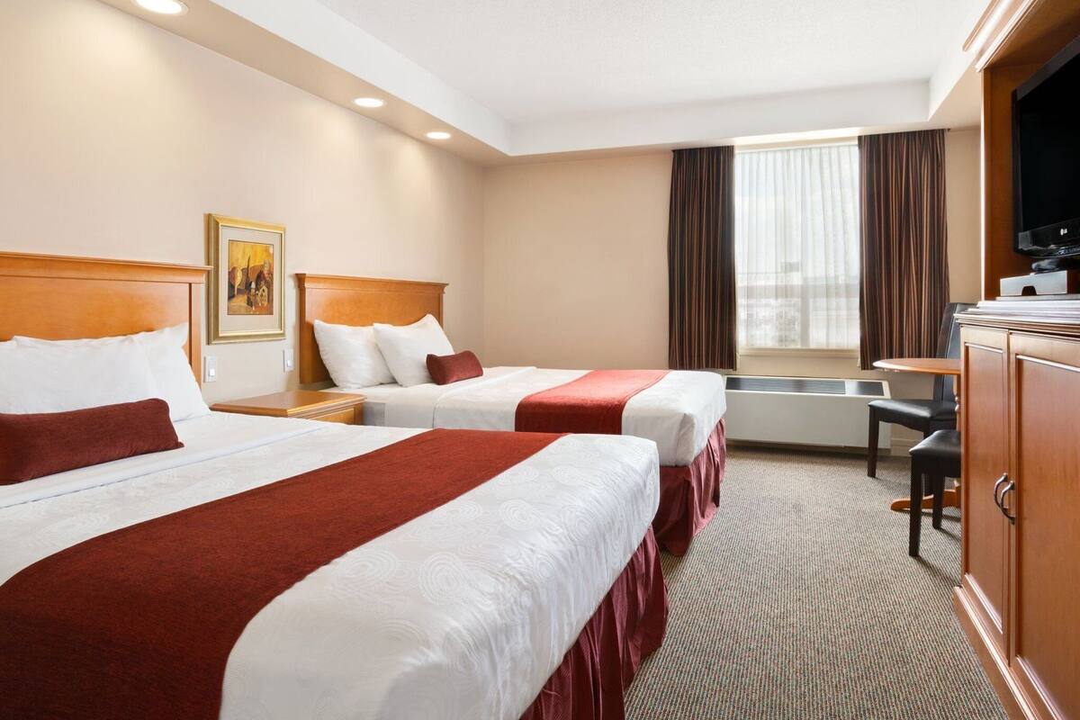 A hotel room with two beds, a desk, a television, and a window with curtains.