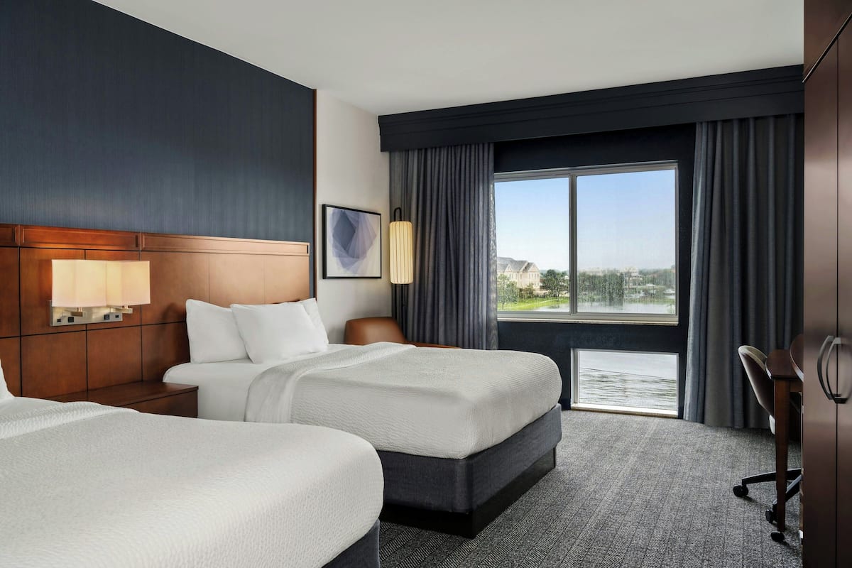 A hotel room with two beds, a large window with a view, a desk, and a chair.