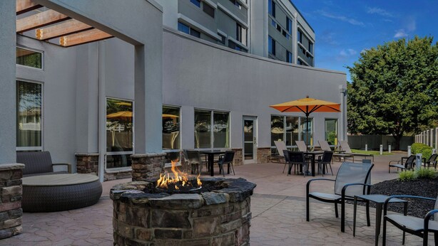 An outdoor patio with stone seating, a fire pit, and tables with umbrellas. - Courtyard by Marriott Evansville East (Evansville)