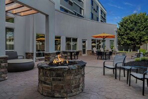 An outdoor patio with stone seating, a fire pit, and tables with umbrellas.