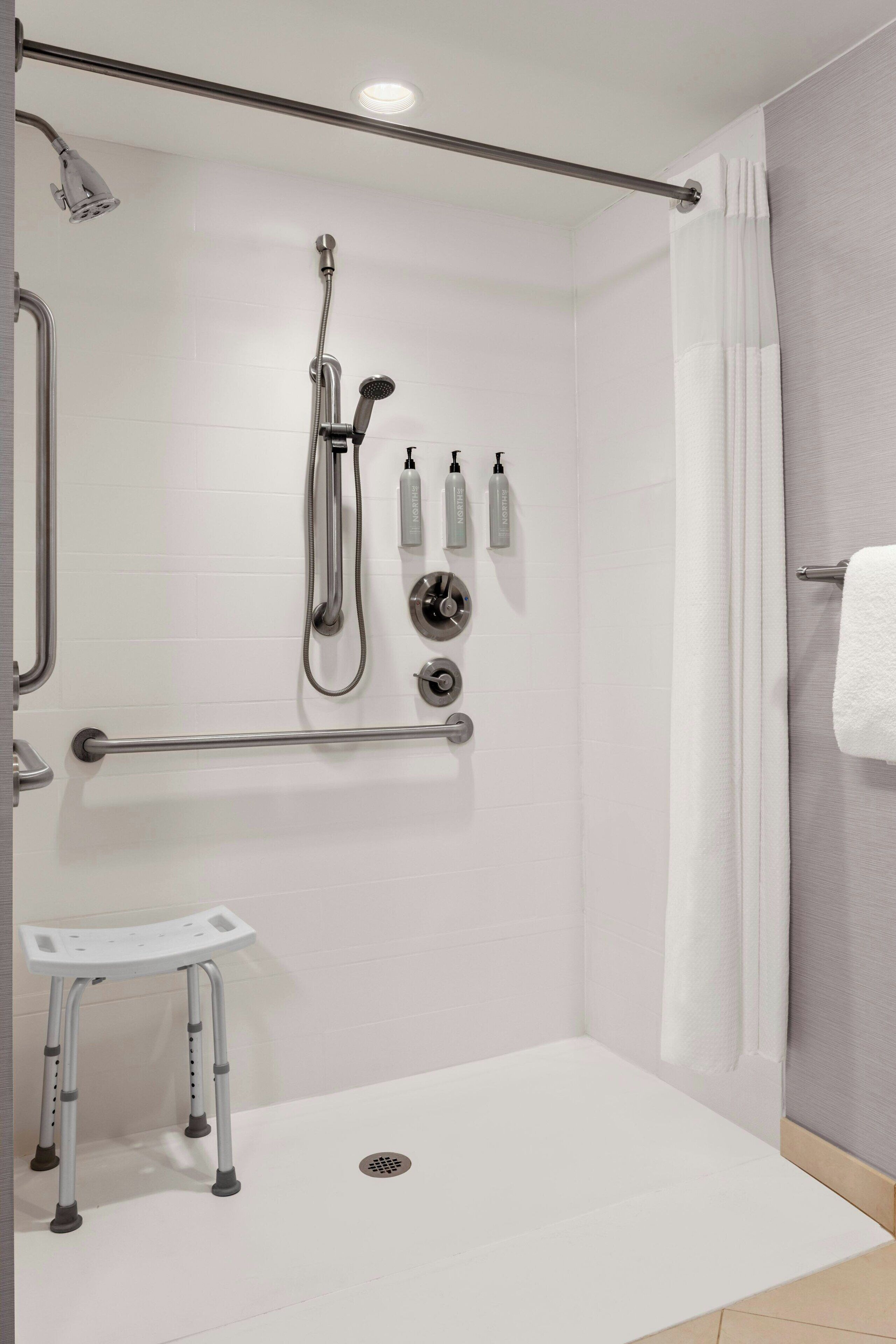 Ein modernes Badezimmer mit barrierefreier Dusche, Haltegriffen, einer Rollstuhlbank und einem Handtuchhalter.