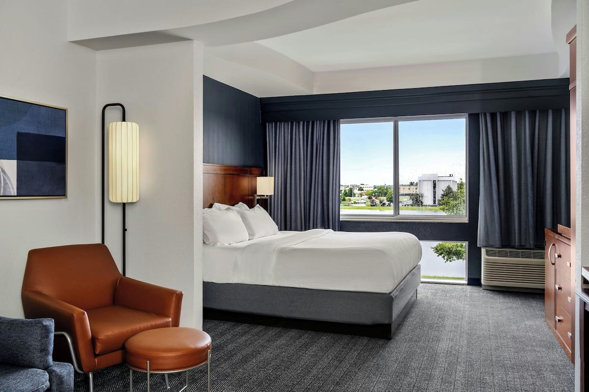 A hotel room with a large bed, a chair, a desk, and a view of the city.