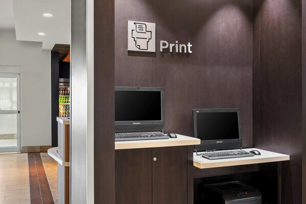 A print station with two computers and a printer, located in a modern office space with a dark wood finish and a tiled floor.