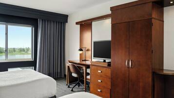 Een hotelkamer met twee bedden, een bureau met een computer, een televisie en een kledingkast.