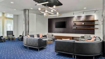 A modern lounge area with a large sectional sofa, a flat-screen TV, and a decorative ceiling light fixture.