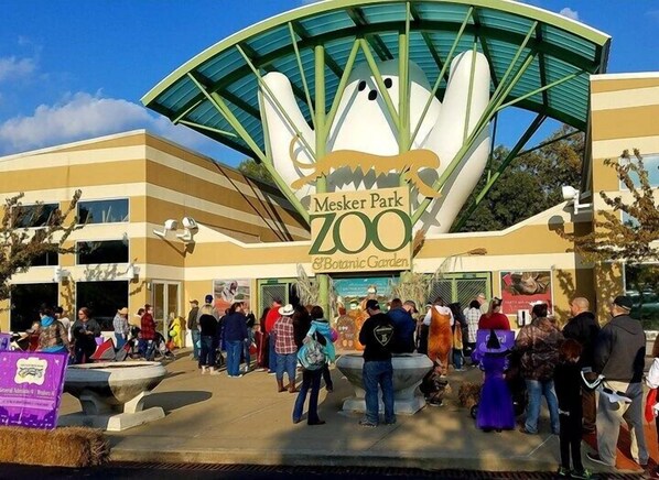 A zoo entrance with a large sign reading "Mesker Park Zoo & Botanical Garden" and a crowd of people in front.