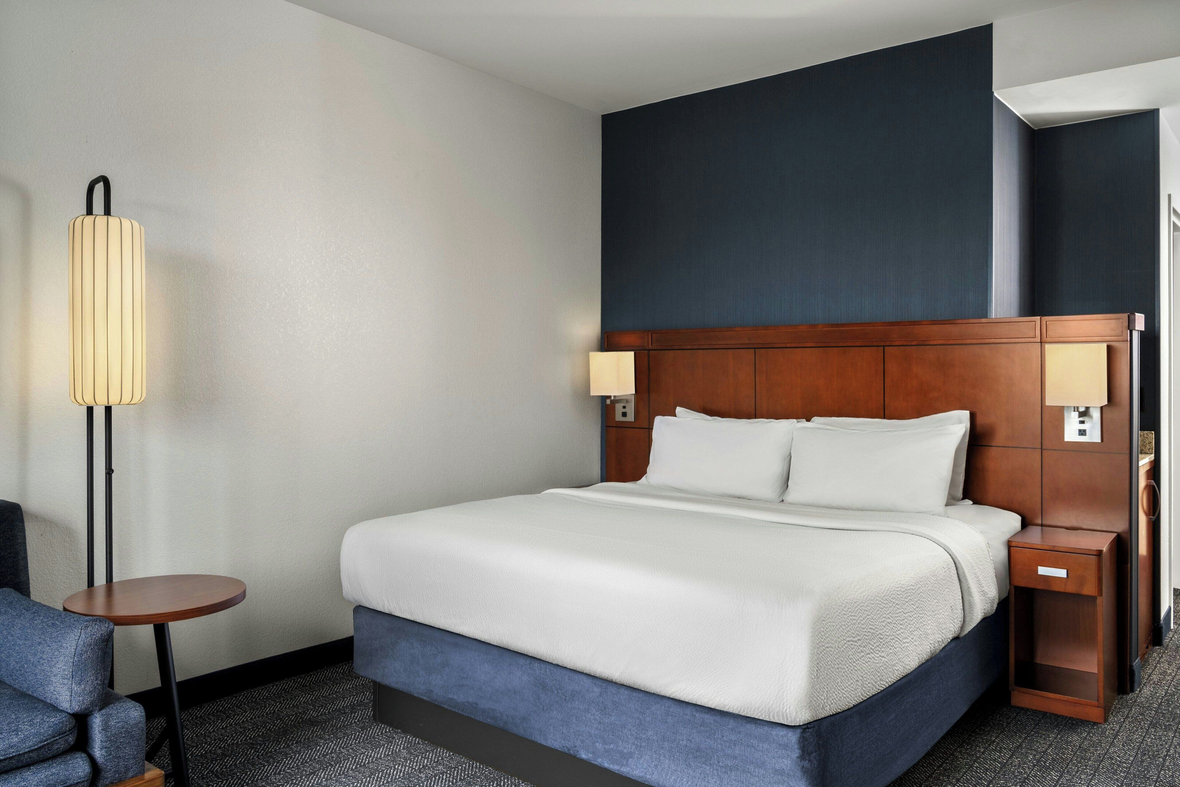 Une chambre d’hôtel avec un grand lit, deux tables de chevet, une chaise et une lampe sur pied.