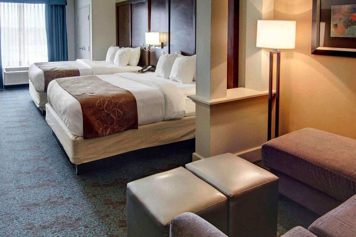 Habitación de hotel con dos camas, un escritorio, una silla, una lámpara y un cuadro en la pared.