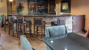 Una zona de bar con taburetes y mostrador, un área de estar con mesa y sillas, y una pared decorativa con una planta.
