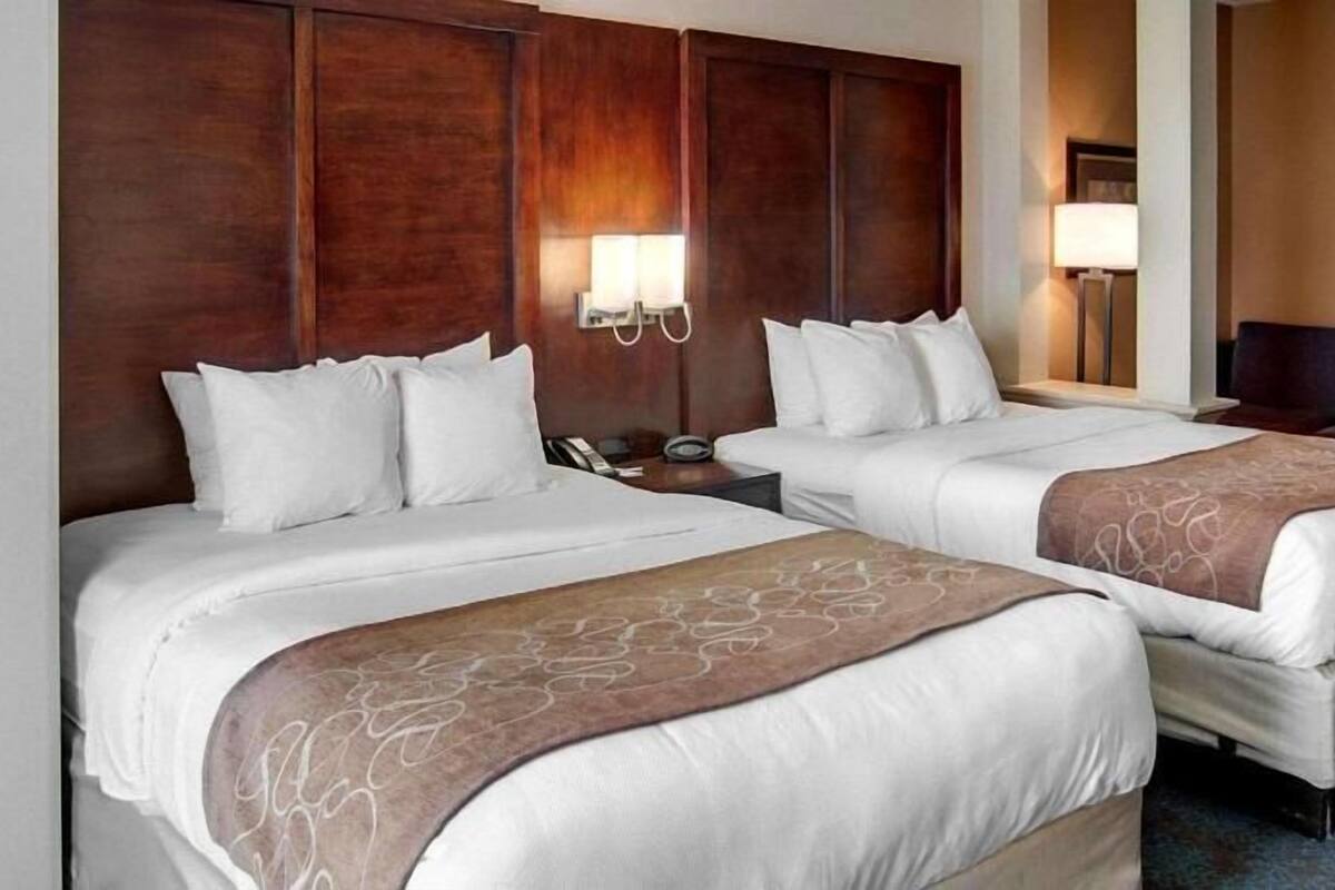 Een hotelkamer met twee bedden, een houten hoofdeinde, bedlampen en een zithoek.