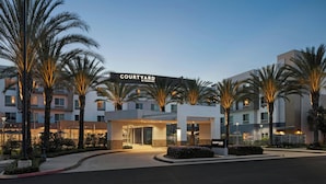 Entrada de un hotel Courtyard by Marriott, con palmeras y un camino de acceso bien iluminado.