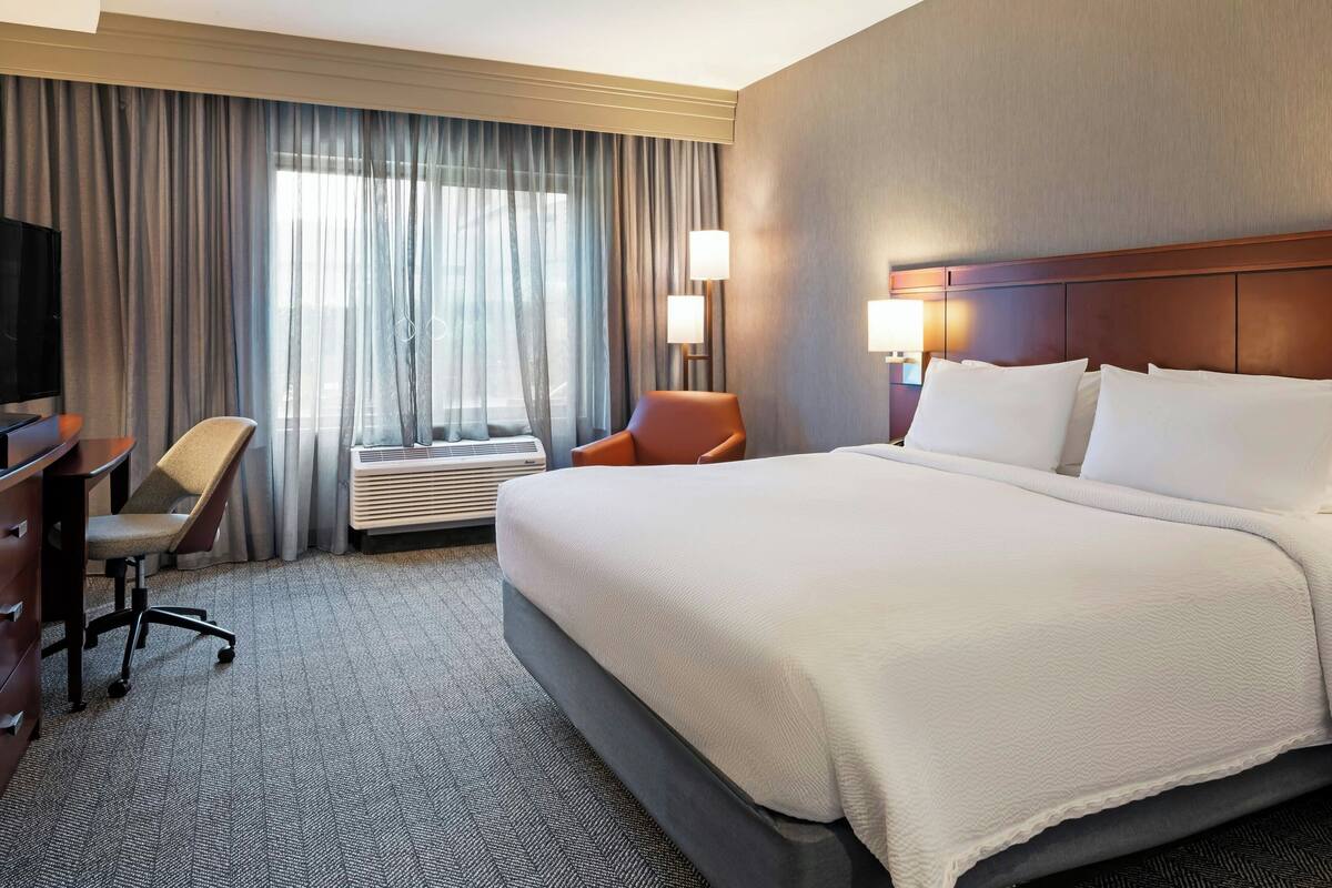 Una habitación de hotel con una cama grande, un escritorio con una silla, un televisor y una ventana con cortinas.