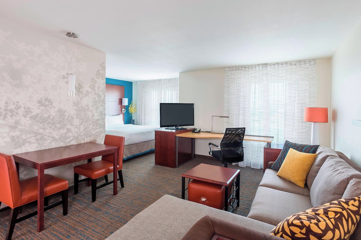 A hotel room with a bed, a desk with a computer, a sofa, and a TV.