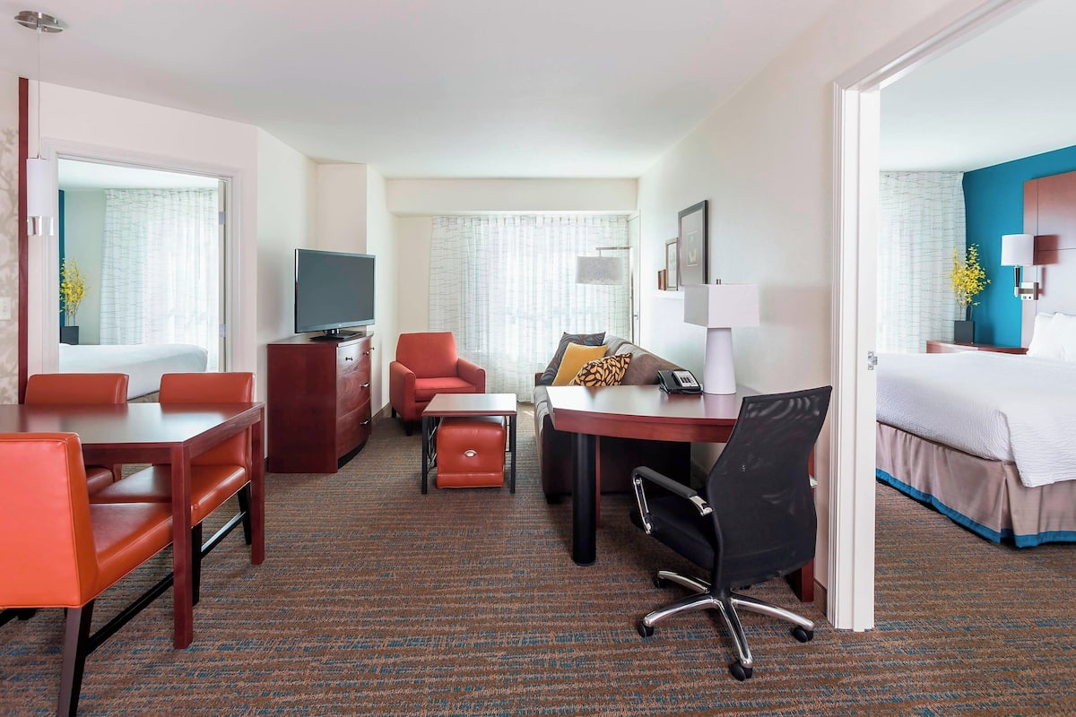 A hotel room with a bed, a desk with a chair, a TV, a sofa, and a small table.
