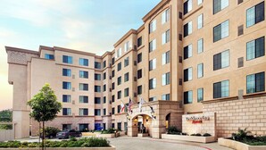 A multi-story hotel with a symmetrical facade, a central entrance with flags, and a landscaped courtyard. - Residence Inn San Diego Del Mar (San Diego)