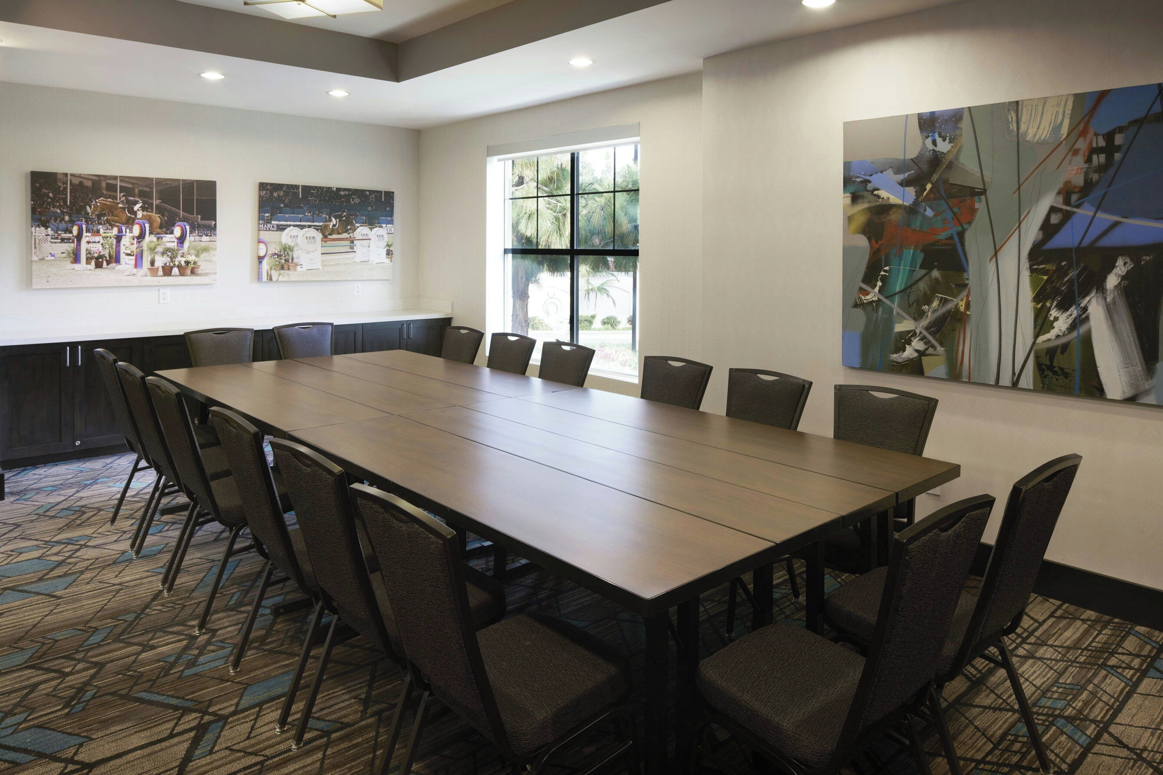 Un salón de conferencias con una larga mesa y sillas, ventanas amplias y obras de arte en las paredes.