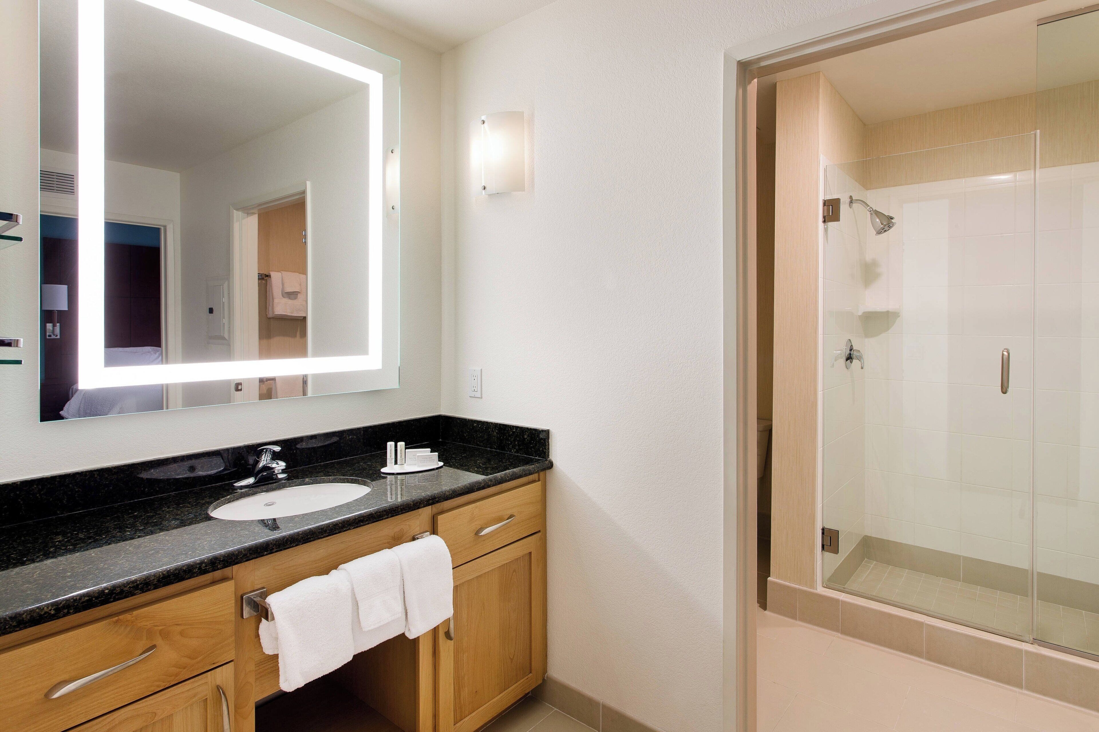 Een moderne badkamer met een grote spiegel, een wastafel, een douche en houten kastjes.