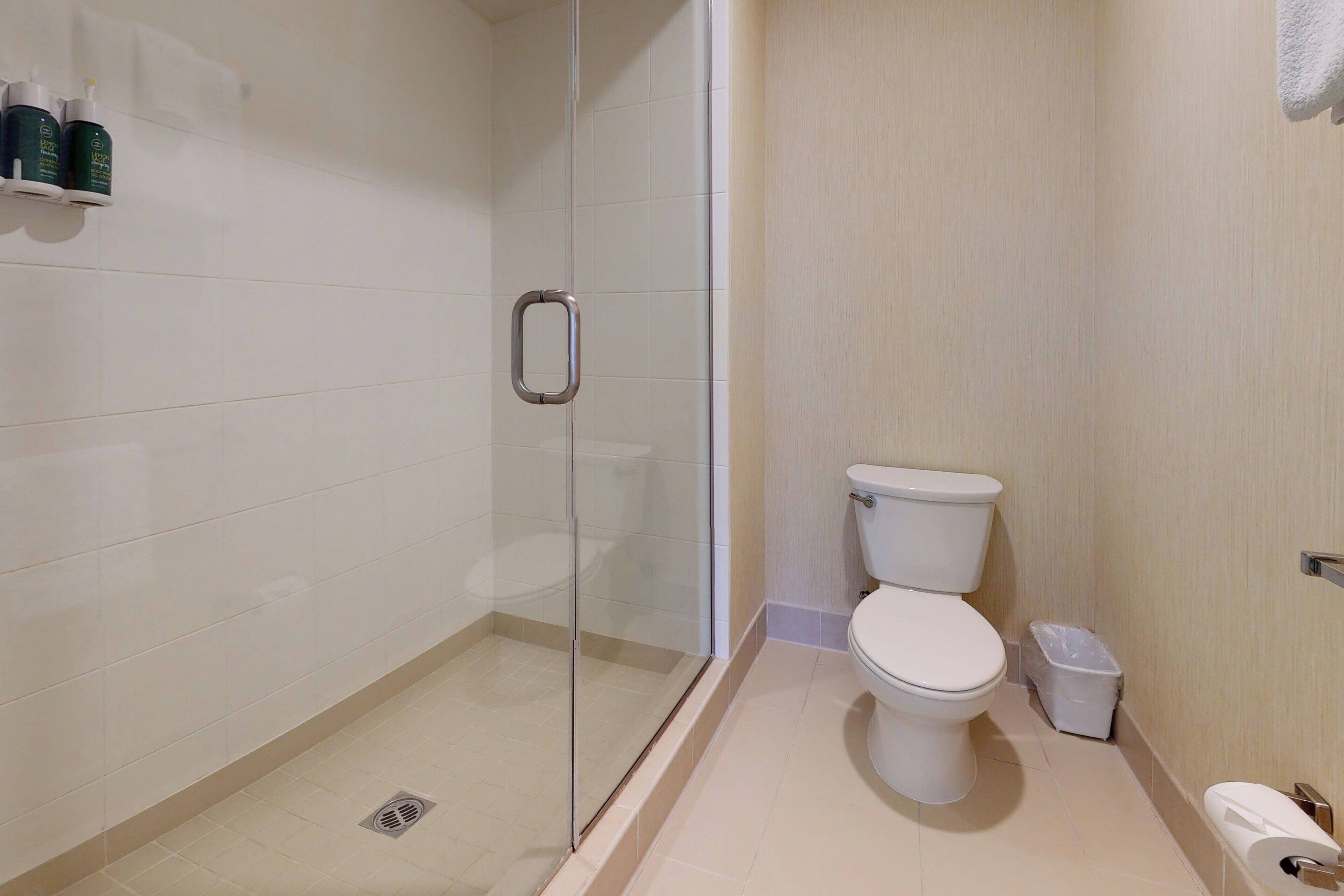 Une salle de bain moderne avec une douche à parois de verre, des toilettes et une poubelle.