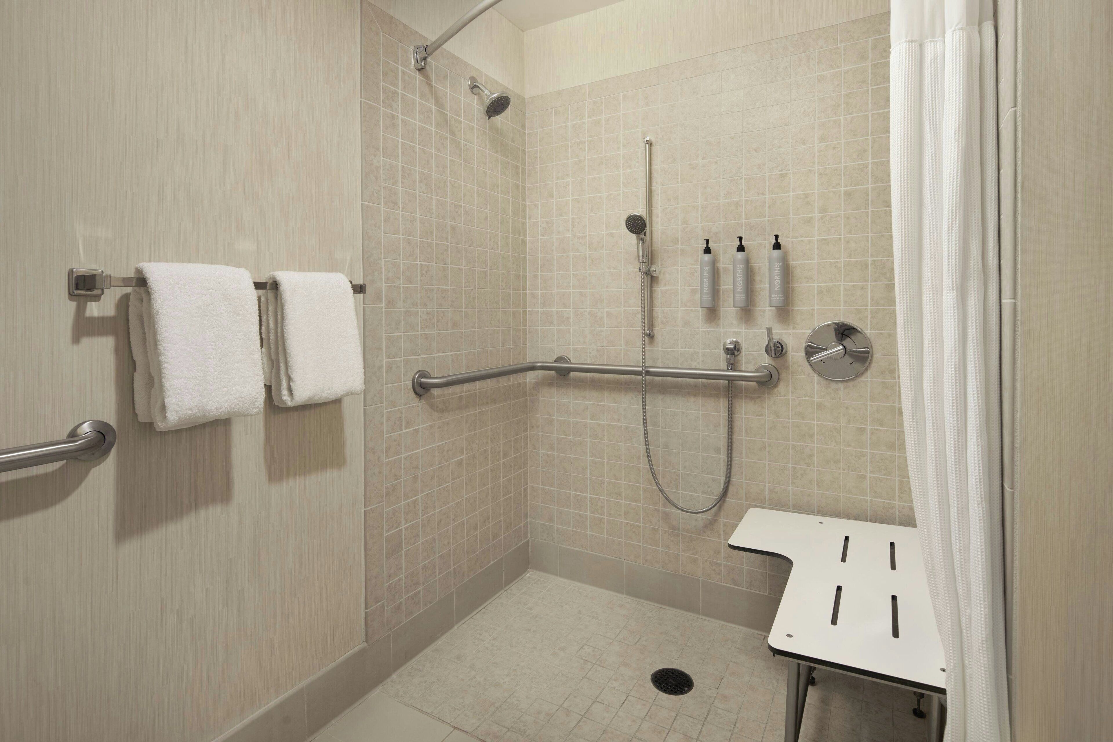 A walk-in shower with beige tiles, a grab bar, a handheld showerhead, and a white sink with a towel rack.