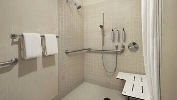 A walk-in shower with beige tiles, a grab bar, a handheld showerhead, and a white sink with a towel rack.