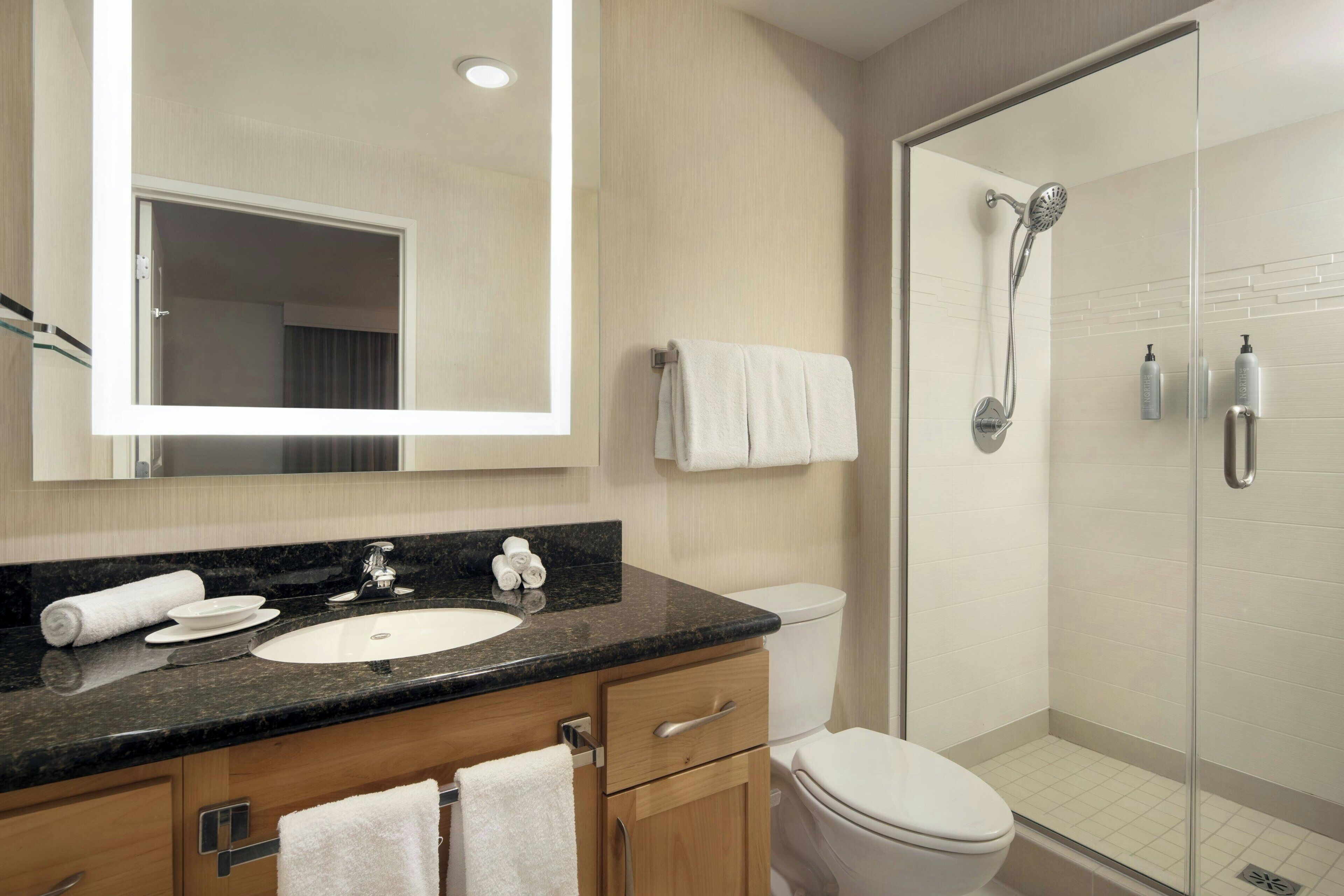Un baño moderno con lavamanos, espejo y ducha.