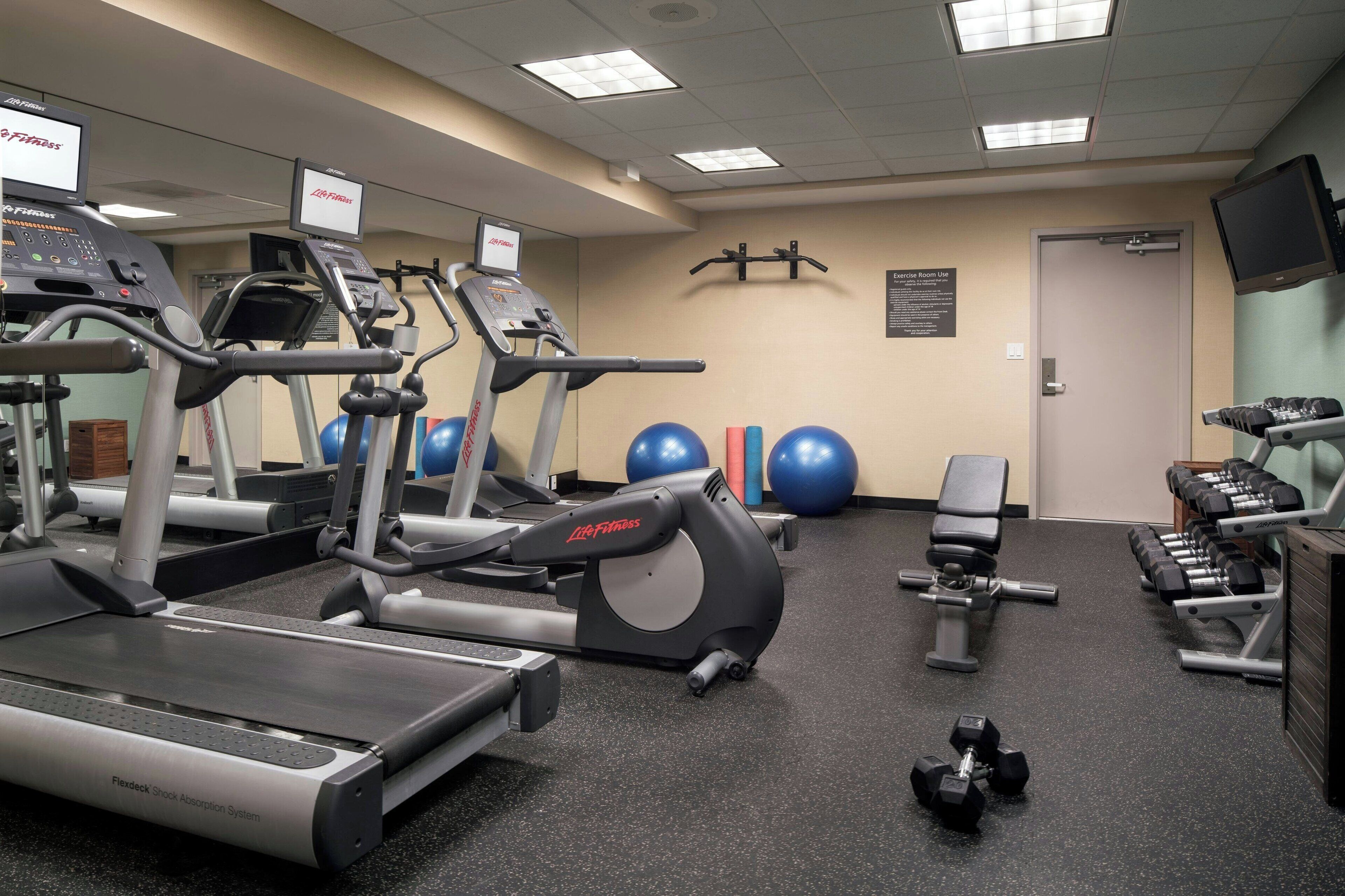 Een fitnessruimte met loopbanden, elliptische trainers, gewichten en trainingsballen.