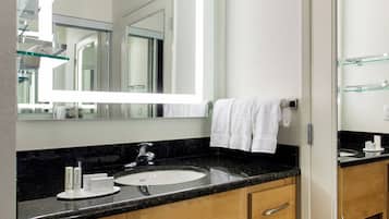 Une salle de bain moderne avec un grand miroir, un plan de toilette noir, des meubles en bois et une étagère en verre.