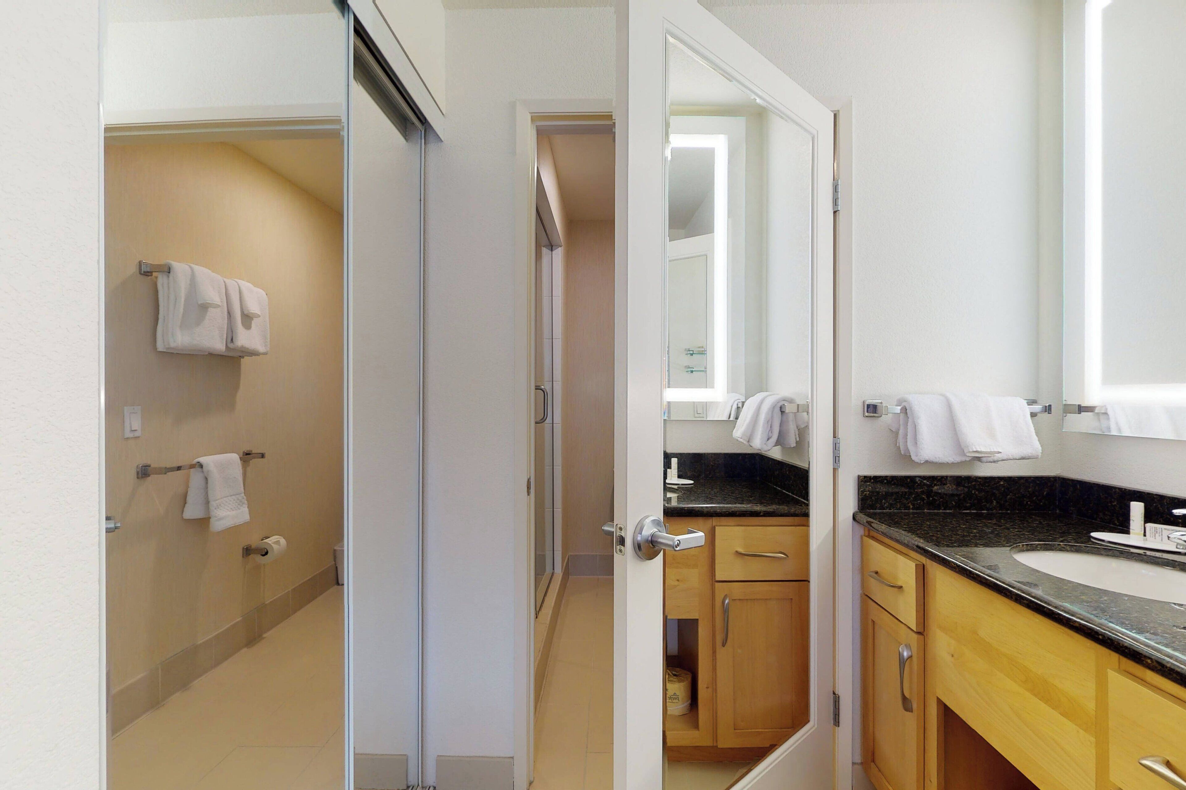 A bathroom with a toilet, sink, and mirror. There are towels hanging on the wall and a shower area visible in the background.
