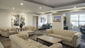 A spacious living area with a large beige sofa set, a coffee table, and a dining table with chairs. There are abstract paintings on the walls and a large window providing natural light. - Residence Inn San Diego Del Mar (San Diego)