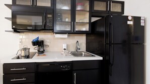 A modern kitchen with black cabinets, a stainless steel microwave, a black refrigerator, and a white countertop. - Candlewood Suites Greeley by IHG (Greeley)