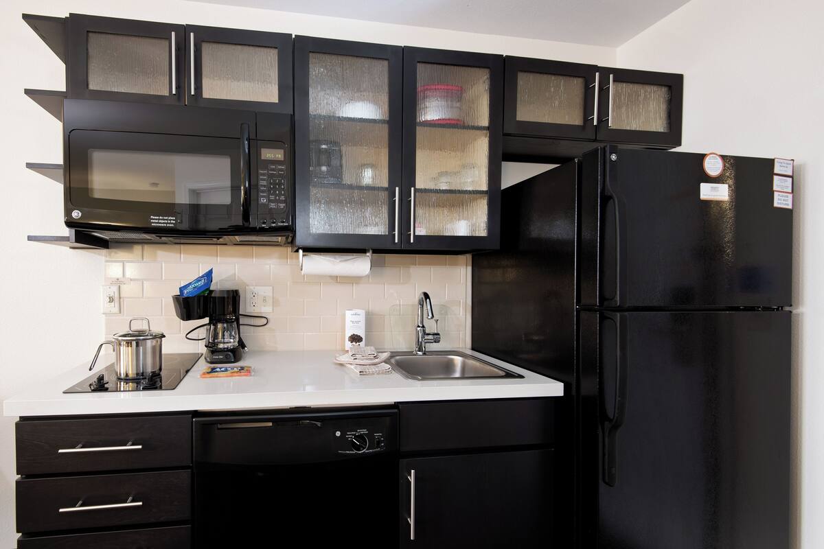 A modern kitchen with black cabinets, a stainless steel microwave, a black refrigerator, and a white countertop.
