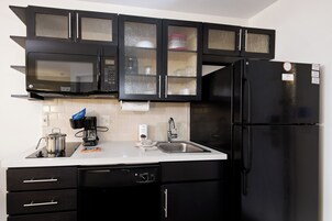 Una cocina moderna con armarios negros, un microondas de acero inoxidable, un refrigerador negro y una encimera blanca.