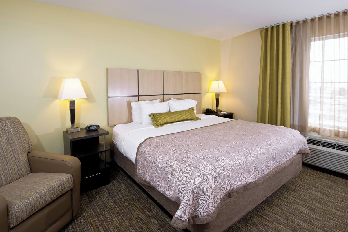 A hotel room with a large bed, two bedside tables with lamps, a chair, and a window with curtains.