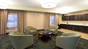 A hotel room with a seating area, a kitchen, and a large window with curtains. - Candlewood Suites Greeley by IHG (Greeley)