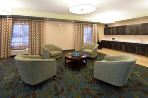 A hotel room with a seating area, a kitchen, and a large window with curtains. - Candlewood Suites Greeley by IHG (Greeley)