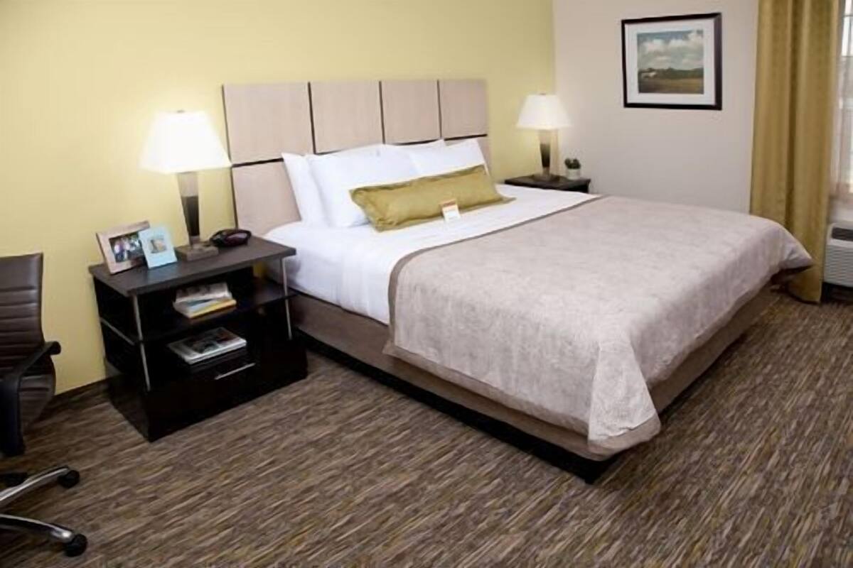 A hotel room with a bed, two bedside tables, a chair, and a framed picture on the wall.