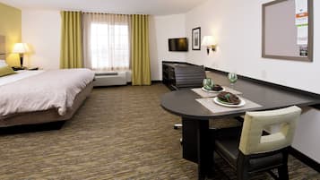 A hotel room with a bed, a desk with a chair, a television, and a bulletin board.