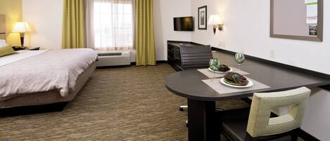 A hotel room with a bed, a desk with a chair, a television, and a bulletin board.