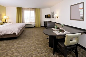 Una habitación de hotel con una cama, un escritorio con una silla, un televisor y un tablón de anuncios.