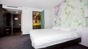 Una habitación de hotel moderna con una cama grande, un vestidor y un baño con cabina de ducha de vidrio.